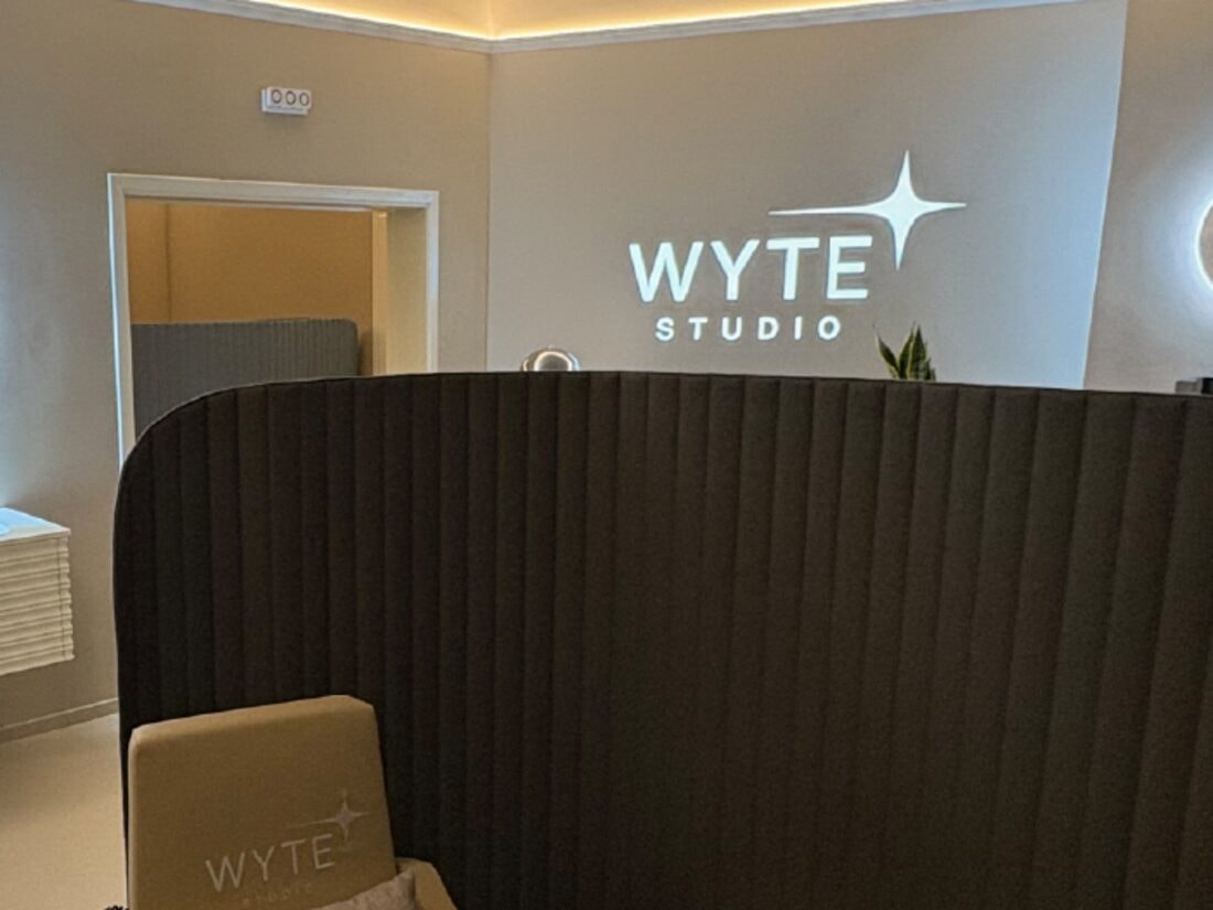 A treatment cabin screened off by a dark acoustic wall, the illuminated WYTE STUDIO sign on the wall behind it.